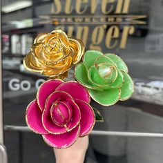 there are three flowers that are in the vase on the window sill and one is pink, green, and gold