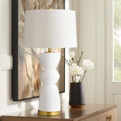 a white lamp sitting on top of a wooden table next to a vase with flowers