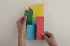 two hands are holding colorful blocks on a white wall and one hand is pointing at them