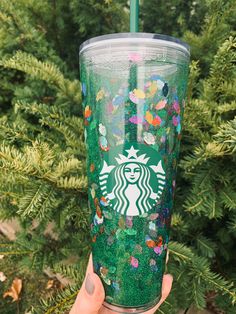 the starbucks cup is decorated with butterflies and glitters, while being held up by someone's hand