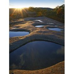 the sun shines brightly over some water in an open area with rocks and grass