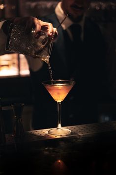 the bartender is pouring an alcoholic drink into a martini glass with a straw in it