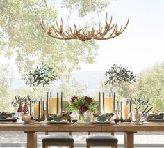 a dining room table with candles, flowers and antlers hanging from it's ceiling