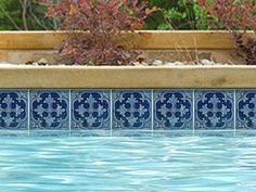 an outdoor swimming pool with blue tiles and plants in the back ground, along with a wooden planter box