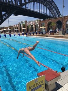 a woman diving into a swimming pool under a bridge