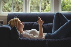 a woman laying on a couch holding a cell phone in her hand and looking at the screen