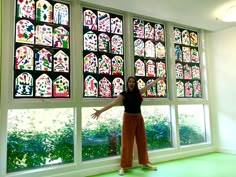 a woman standing in front of a window with many stained glass windows behind her and arms outstretched