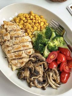 a white plate topped with chicken, mushrooms, tomatoes and broccoli next to corn