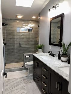 a bathroom with two sinks, a toilet and a walk in shower area that has gray tiles on the walls