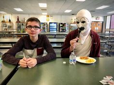 two people sitting at a table with food in front of them and one person wearing a mask