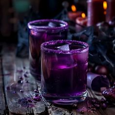 two glasses filled with purple liquid sitting on top of a wooden table next to candles