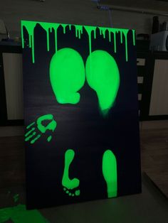 a painting with green paint on it in the middle of a room, depicting two feet and one hand