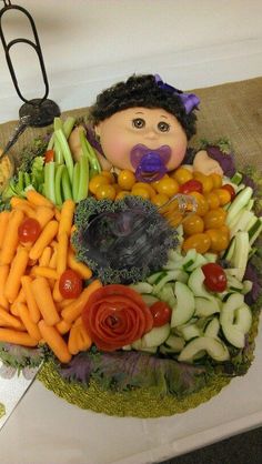 an arrangement of fruits and vegetables with a doll in the middle