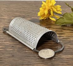 a coin is sitting on a table next to a metal grater and yellow flowers