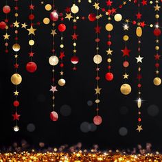 gold and red christmas decorations hanging from strings on a black background with lights in the foreground