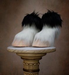 black and white furry slippers sitting on top of a pedestal