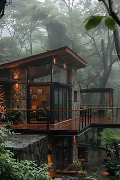 a house in the middle of a forest with trees and bushes around it, surrounded by fog