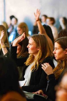 a group of people sitting next to each other in a room with their hands up