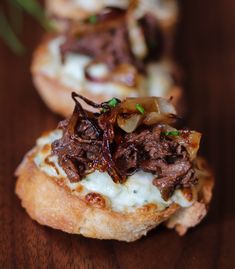 three small pastries with meat and cheese on them sitting on a wooden table top