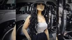 a woman with long black hair wearing a hat and standing in front of a car