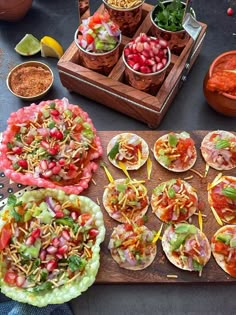 several tacos are arranged on a cutting board with bowls of salsa and condiments