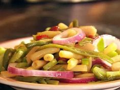 a white plate topped with green beans, onions and red onion salad on top of a wooden table