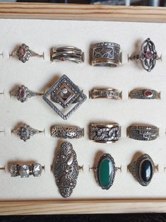 a collection of various rings in a wooden display case on top of a white surface