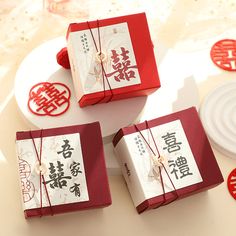 three red and white boxes with chinese writing on them sitting on a table next to plates