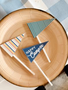 two happy campers pennants on top of a wooden plate with blue and white striped flags