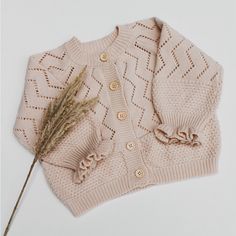 a knitted sweater with a flower on the side and a dried plant in front