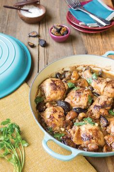 a pan filled with chicken and mushrooms on top of a wooden table next to plates