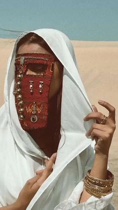 a woman in white is covering her face with a red mask and jewelry on it