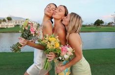 three beautiful women kissing each other in front of a body of water with flowers and greenery