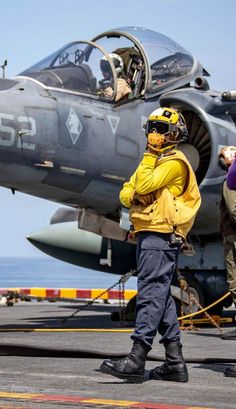 a fighter jet sitting on top of an airport tarmac next to the ocean with people standing around it