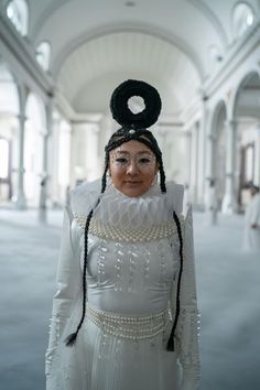 a woman in a white dress and black headdress standing in a building with arches on the ceiling