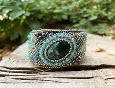 a green bracelet sitting on top of a piece of wood next to some trees and bushes