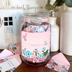 a jar filled with pink and blue flowers sitting on top of a table next to envelopes