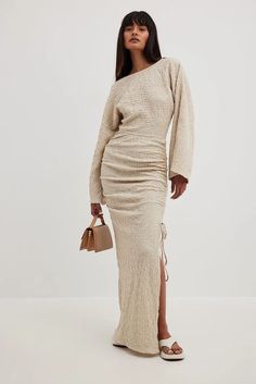 a woman in a beige sweater and long skirt standing with her hand on her hip