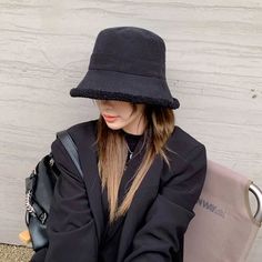 a woman wearing a black hat sitting on top of a chair next to a wall