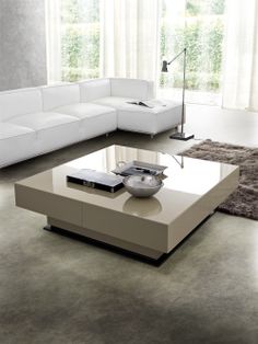 a modern living room with white couches and a coffee table in front of a large window