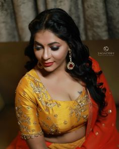 a woman in a yellow and red sari sitting on a couch with her hands clasped to her chest