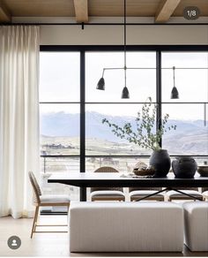 a dining room table and chairs with large windows looking out onto the mountains outside in front of them