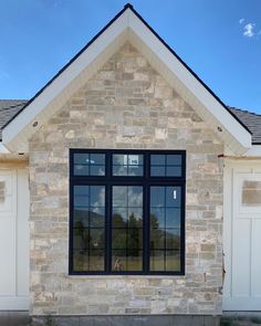 a stone house with black windows and white shutters on the front door is shown