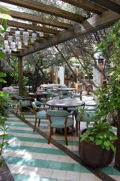 an outdoor dining area with blue chairs and green plants on the tables, surrounded by greenery