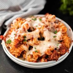 a white plate topped with pasta covered in cheese and sauce on top of a table