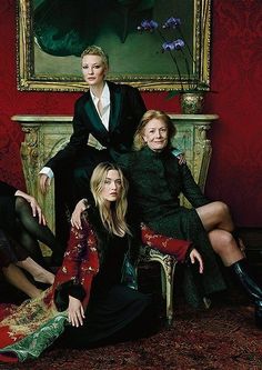 three women are sitting on a chair in front of a painting and another woman is standing next to her