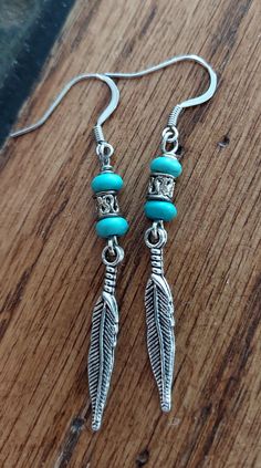 the earrings are made from silver and turquoise beads with feathers hanging from them on a wooden surface