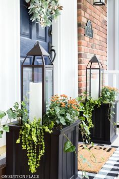 two black planters filled with plants on the front porch