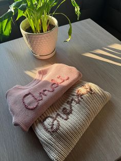 two knitted sweaters sitting on top of a table next to a potted plant