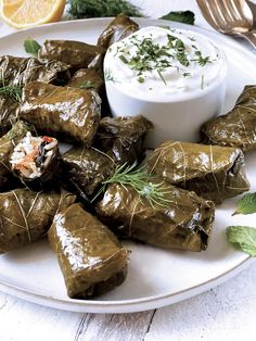 a white plate topped with stuffed grape leaves next to a bowl of yogurt